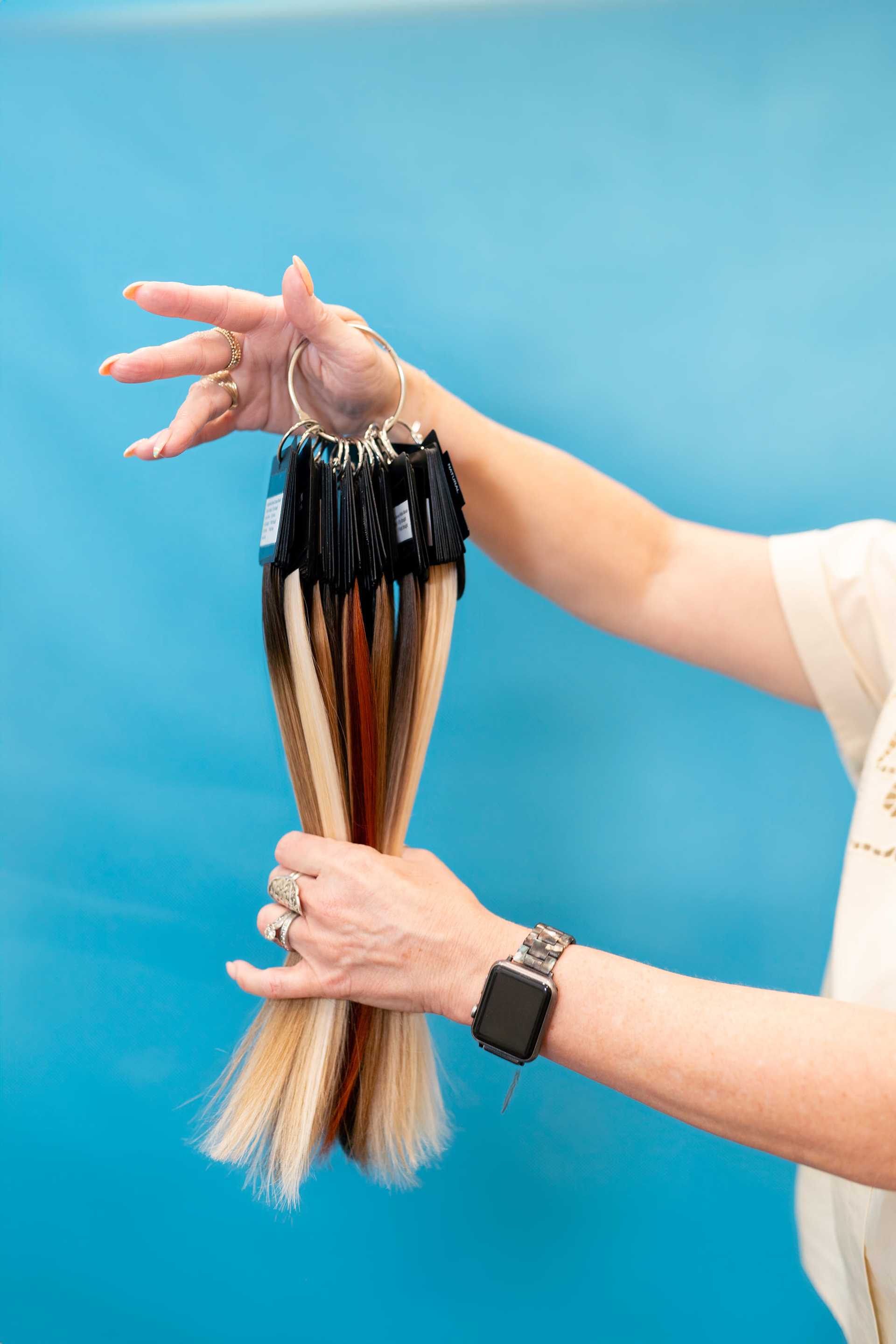 Colorful hair extension samples held in a hand against a blue background.