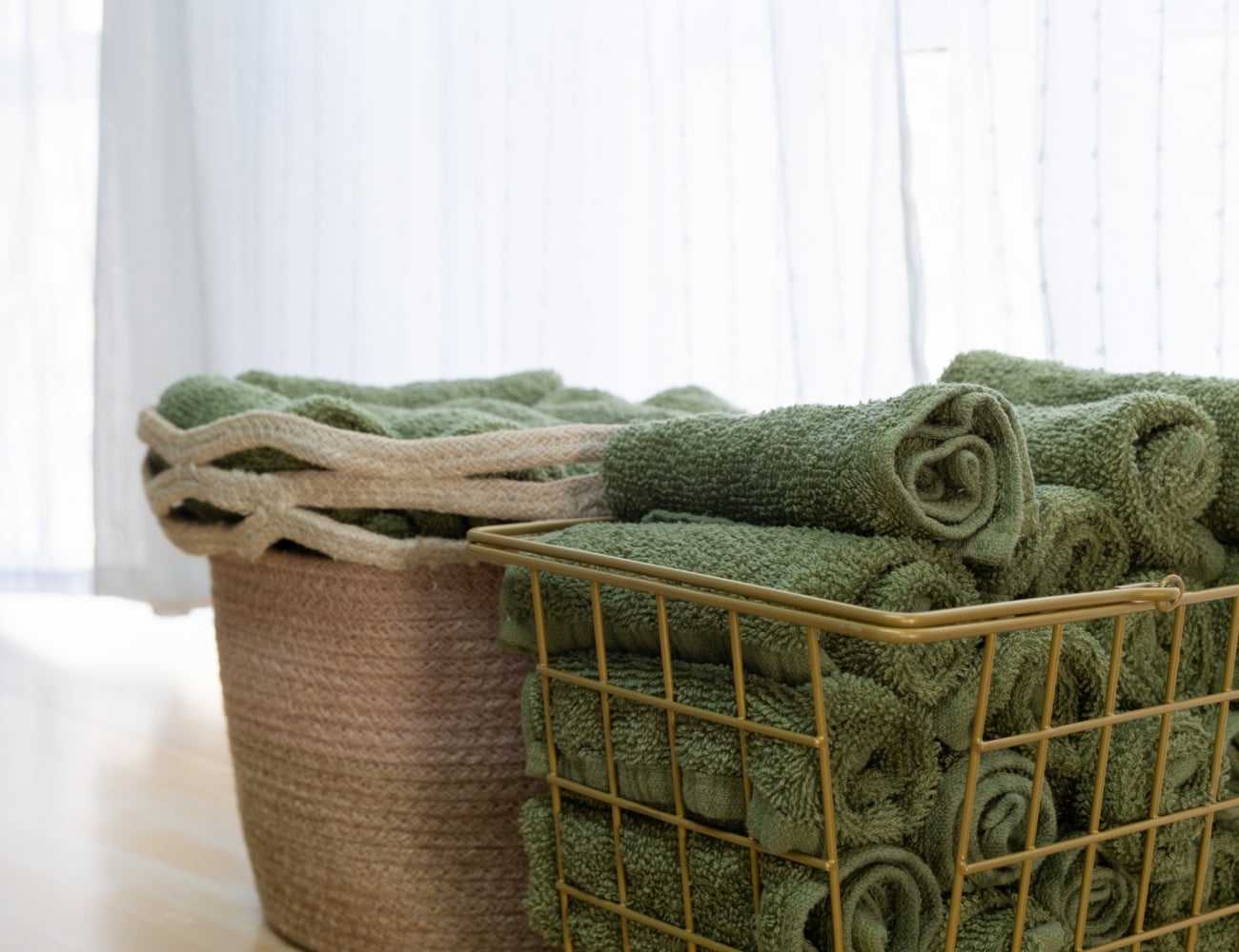 Green towels neatly rolled in baskets by a soft-lit window.