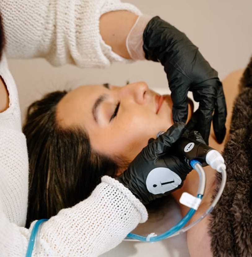 Person receiving a facial treatment with a skincare device and black gloves.