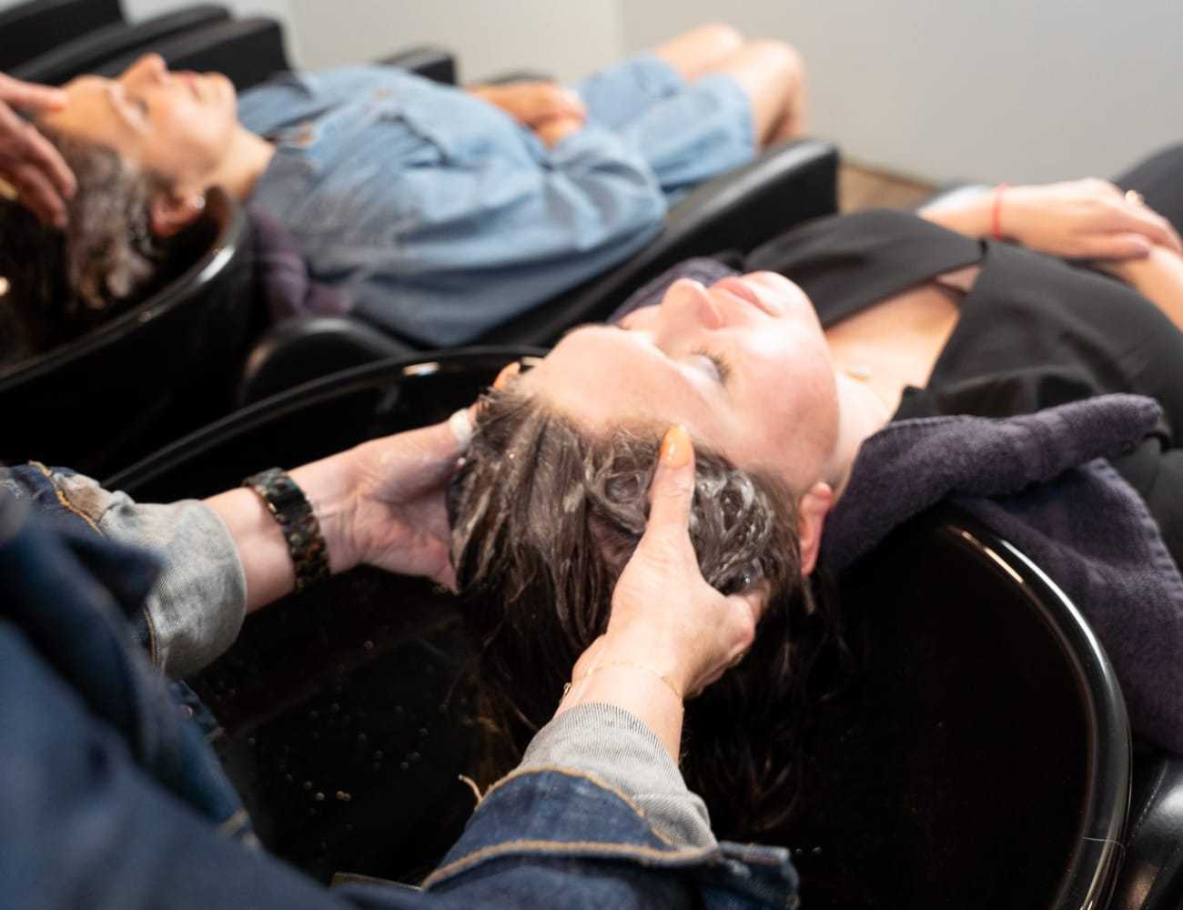 Two people getting hair washed at a salon, stylist massaging shampoo into hair.